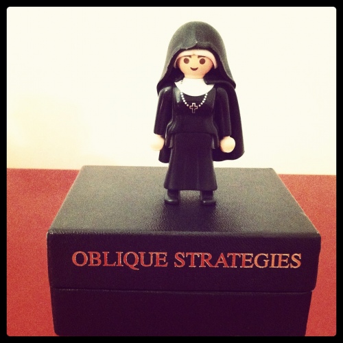 a figurine of a nun standing on Brian Eno's Oblique Strategies game.